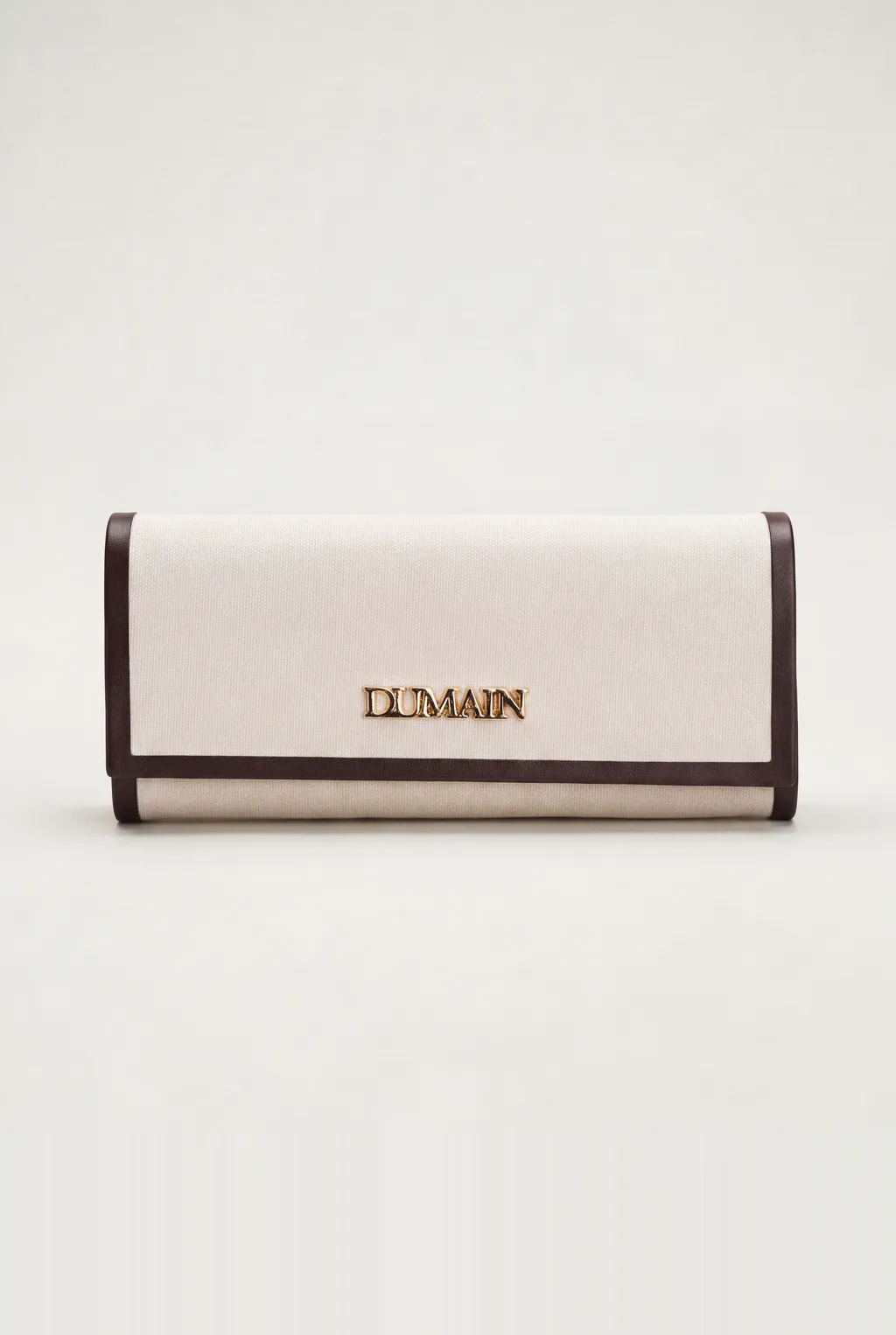 Cream canvas clutch with dark leather trim and a gold DUMAIN logo