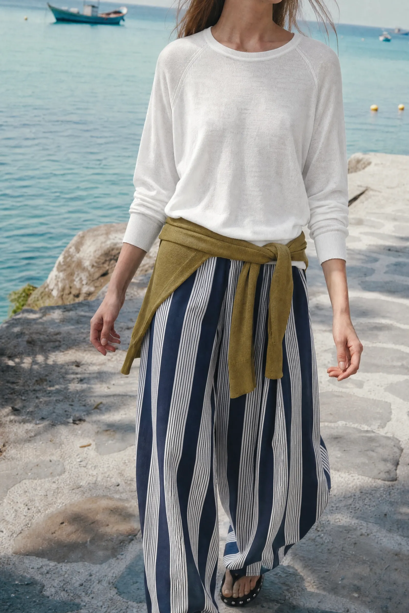Model walking along a seaside promenade in a white top and navy striped wide-leg trousers