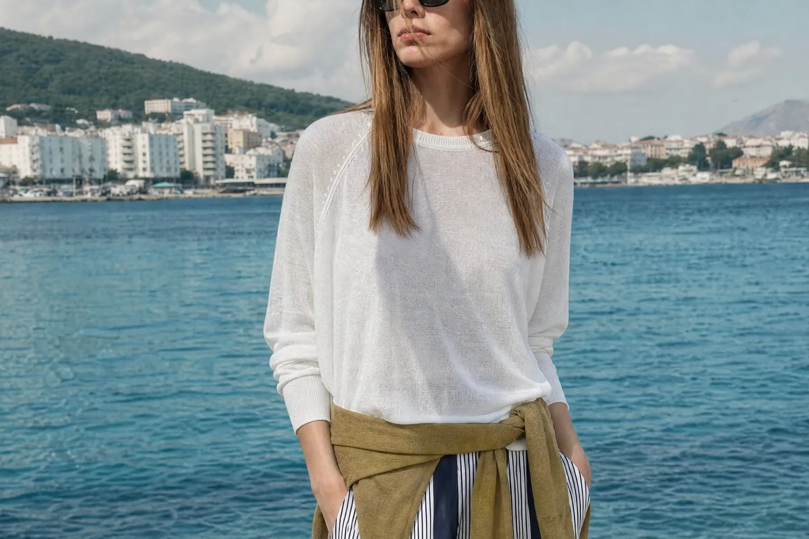 Model by the water in a white top with an olive tie and navy striped trousers