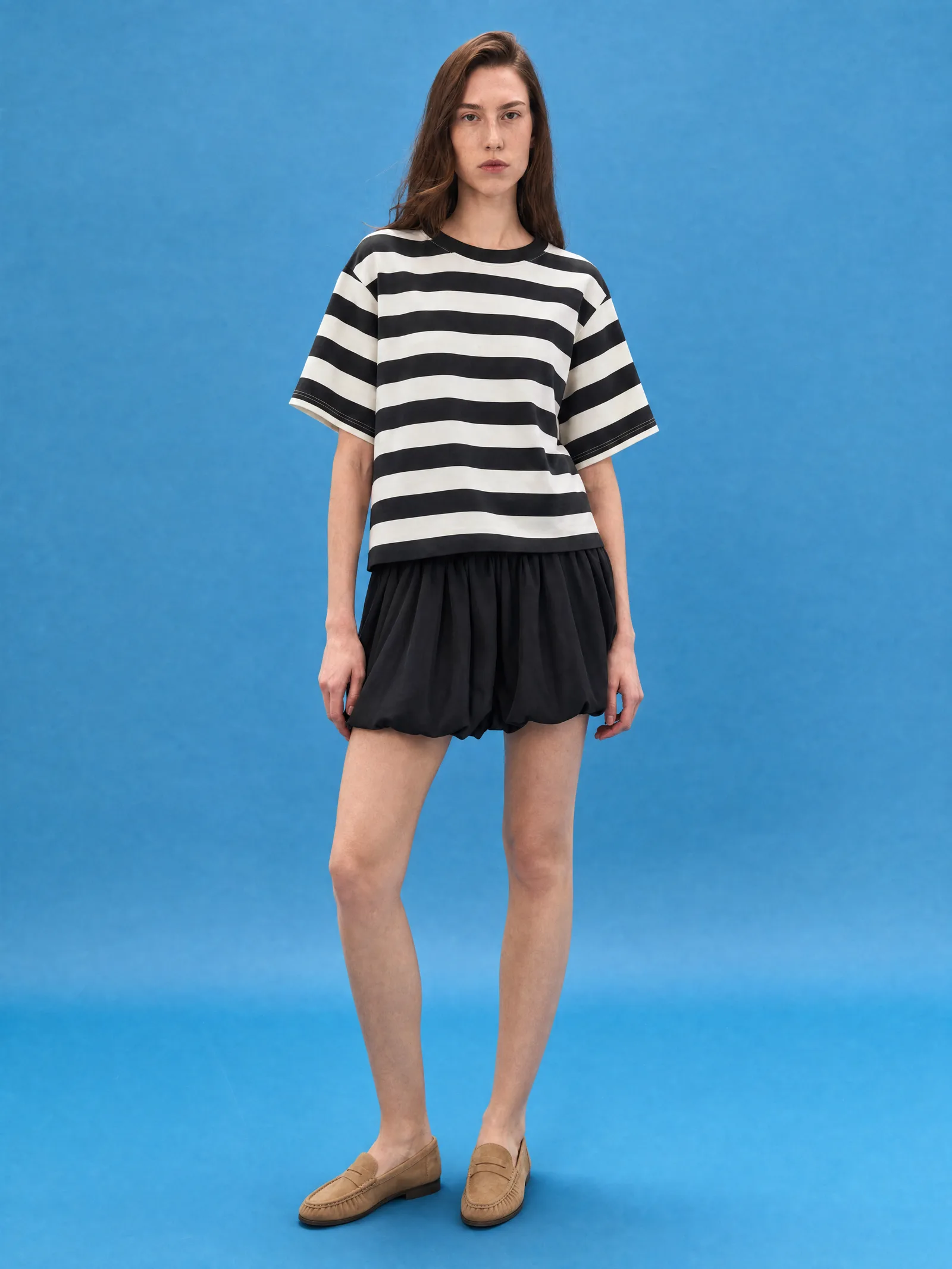 Delucca Spring Collection: model in a black-and-white striped tee and black bubble skirt against a blue backdrop